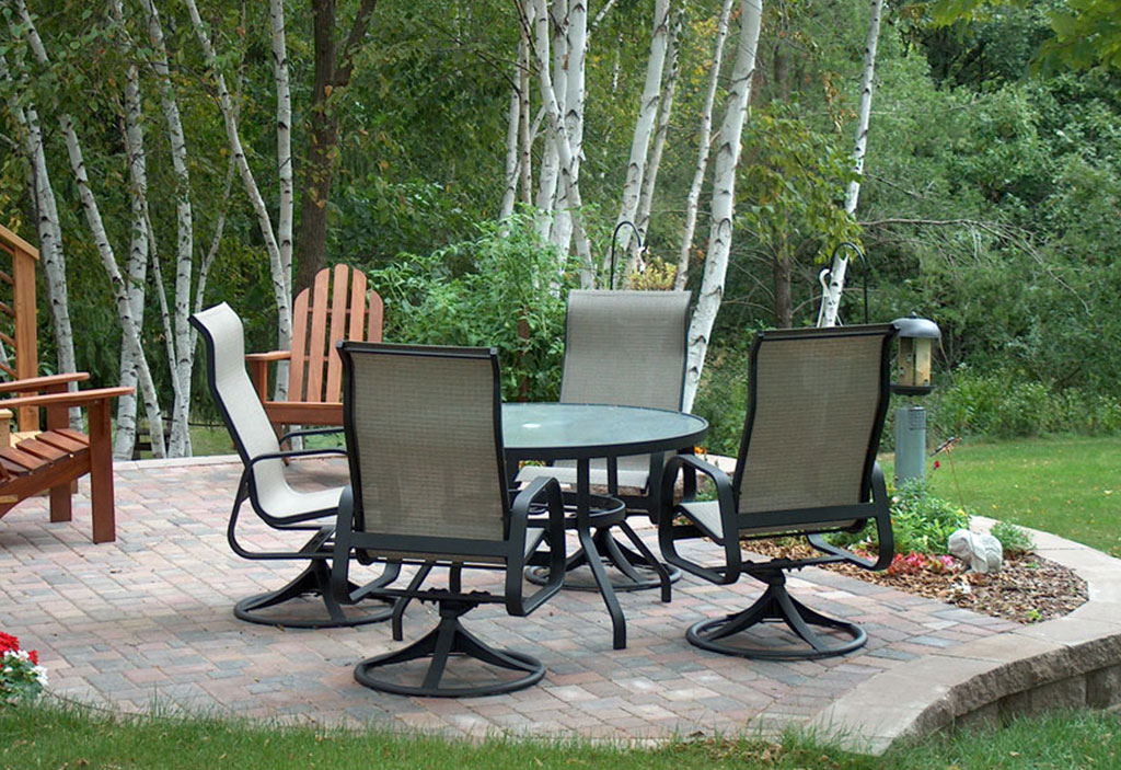 A beautiful stone patio with a table and chairs, surrounded by trees.